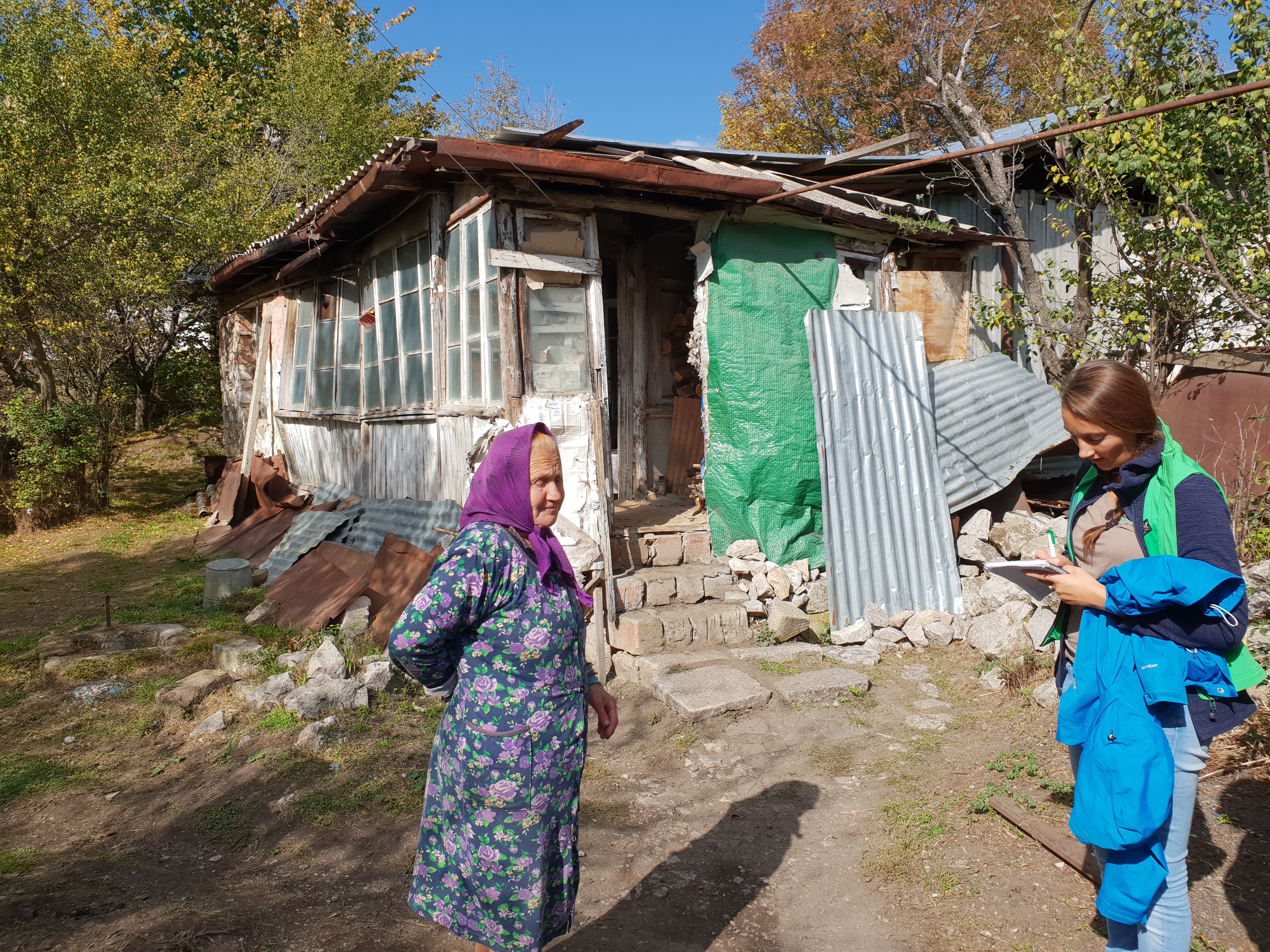 Sie steht vor den Trümmern, die sie ihr Zuhause nennt. Die 80-jährige Mariam Gnasian erzählt Hoffnungszeichen-Mitarbeiterin Ildiko Mannsperger von ihrem Leben in großer Armut.
