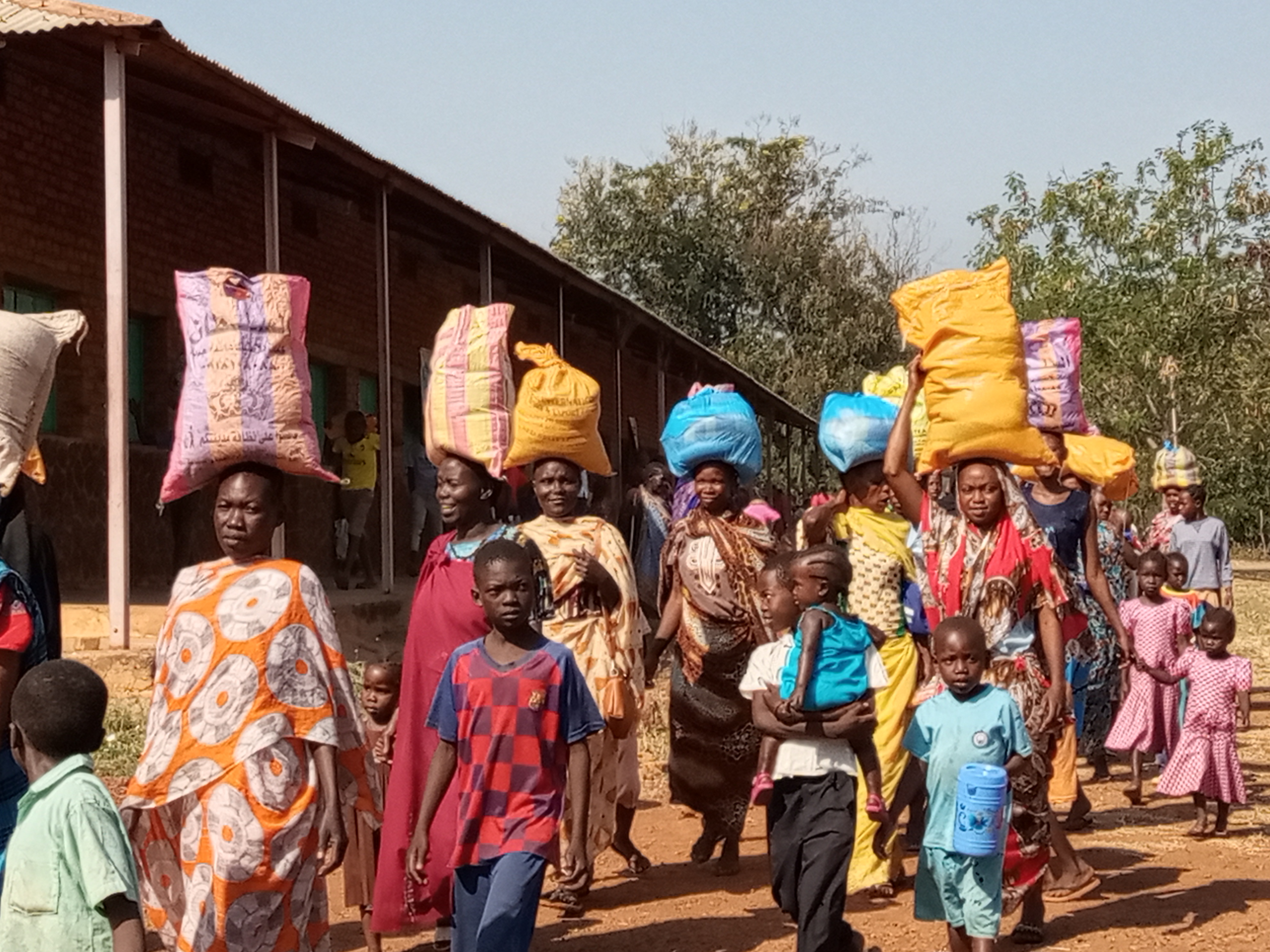 Wie in einer fröhlichen Prozession ziehen die Frauen und Kinder mit ihrem Hilfspaket nach Hause. Viele mangelernährte Kinder erhalten so dank unserer Spender  wieder ausgewogenere und nahrhaftere Mahlzeiten.