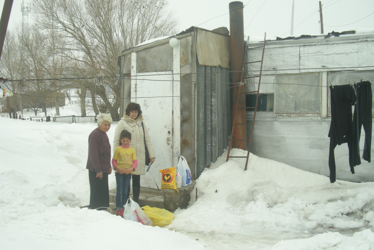 Die Behausungen vieler Menschen sind elend – Kälte und Nässe dringen ein.  Geld für Nahrung, Kleidung oder Feuerholz fehlt oft. Unsere Helferin (hinten)  bringt auch dieser Familie ein Hilfspaket.