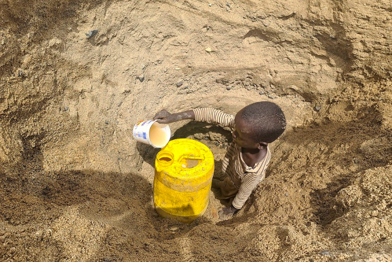 Ein Kind aus dem Bezirk Illeret im Norden Kenias schöpft das letzte Wasser aus einem selbst gegrabenen Wasserloch.