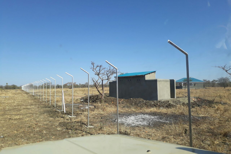 Baufortschritt in Kosike: Das Gelände ist vorbereitet, Zaunpfosten stehen, die ersten Latrinen sind errichtet (Mitte). Auch der Rohbau des Büro- und Lagerhauses ist fertig (hinten rechts). Auf dem Gelände leistet unser Team schon jetzt zweiwöchentlich medizinische Versorgung.