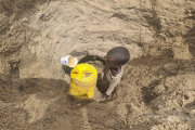 Ein Kind schöpft das letzte Wasser aus einem Wasserloch.