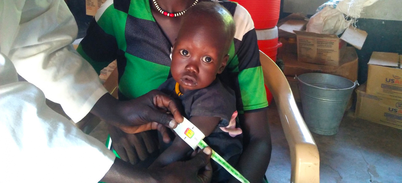 Ein mangelernährtes Kind wird in der Klinik der Diözese Rumbek untersucht. Der Umfang seines Oberarms misst ein Ernährungsberater mit einem speziellen Maßband, um das Ausmaß der Unterernährung zu erfassen.