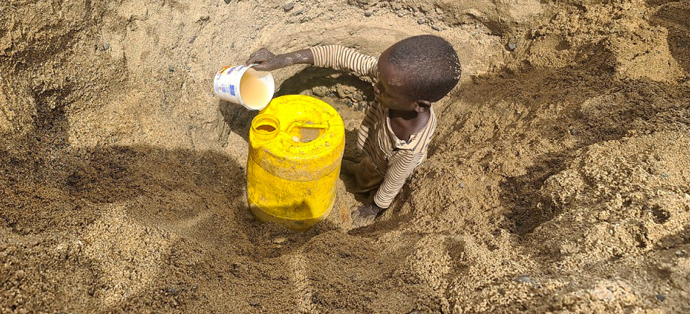 Ein Kind aus dem Bezirk Illeret im Norden Kenias schöpft das letzte Wasser aus einem selbst gegrabenen Wasserloch.